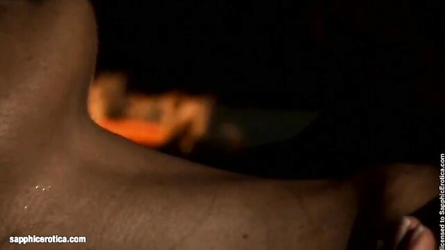 Attractive lesbians necking passionately by firelight in dark room