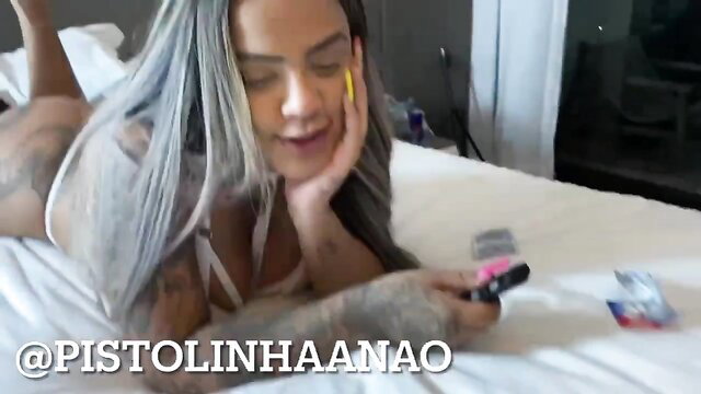 Tattooed latina with silver hair in lingerie on bed holding pink toy