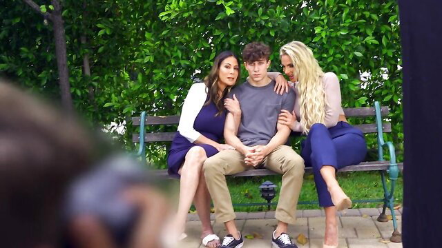 Curvy brunette and blonde MILFs flank young guy on park bench BTS