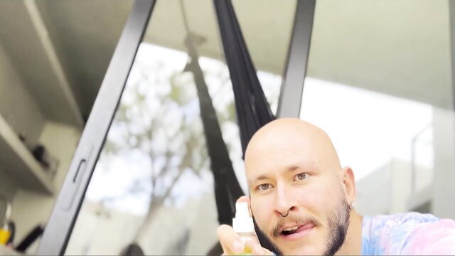 Bald hunky guy holds lotion bottle, close-up face in bright room