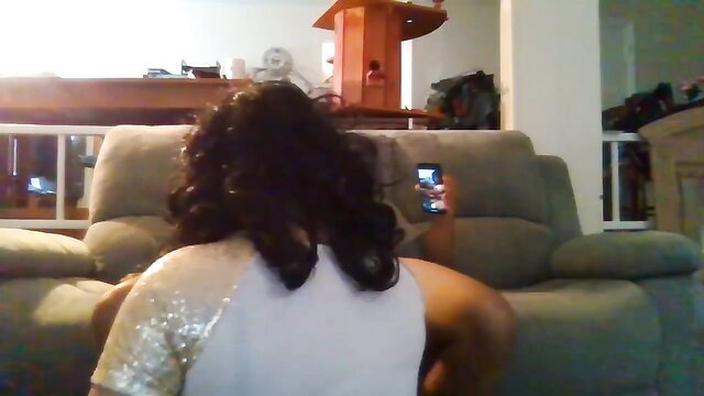 Black woman in sparkly top sits on couch holding phone, amateur adult thumbnail