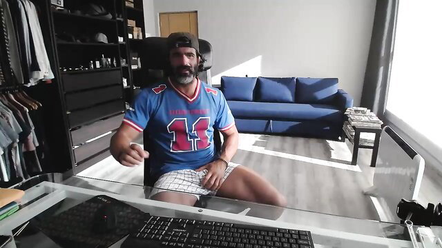 Handsome Latino man in football jersey and shorts at desk, sexy pose