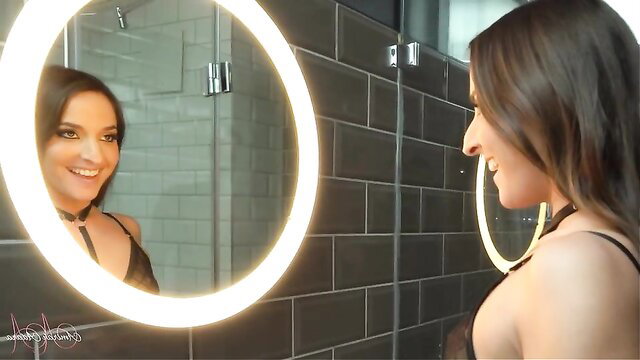 Amirah Adara smiling in mirror, black lingerie choker in bathroom