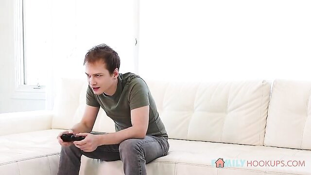 Guy gaming on couch in tight tee and jeans, horny stepmom hookup vibe