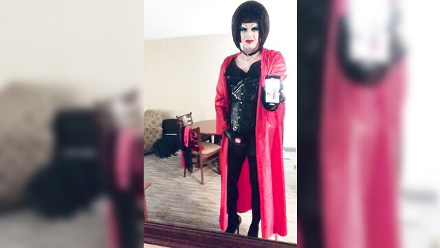 Enormous makeup sissy in red PVC robe and black corset posing in hotel room