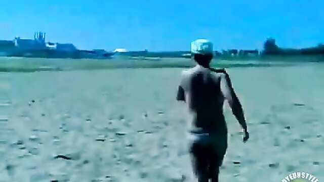 Nude man walking on beach with topless women in background