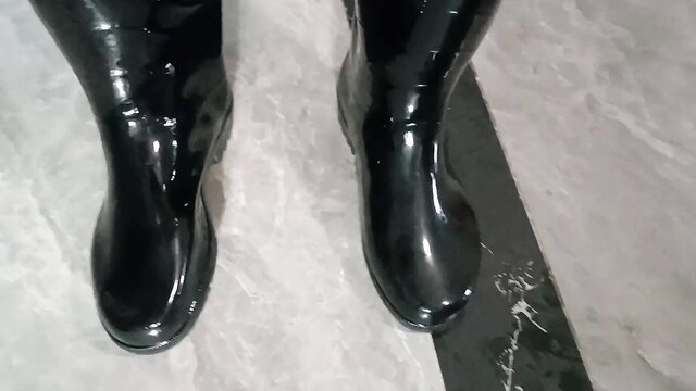 Shiny black knee-high rubber boots closeup in fetish pose