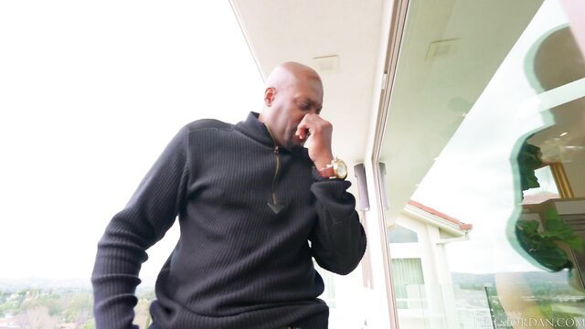 Bald black man in black turtleneck wiping eyes on balcony