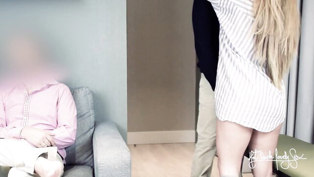 Blonde wife in striped dress stands over fan as pink hoodie hubby watches cuckold fuck