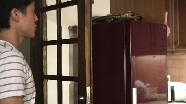 Frustrated Asian wife peeking at brother-in-law by kitchen fridge