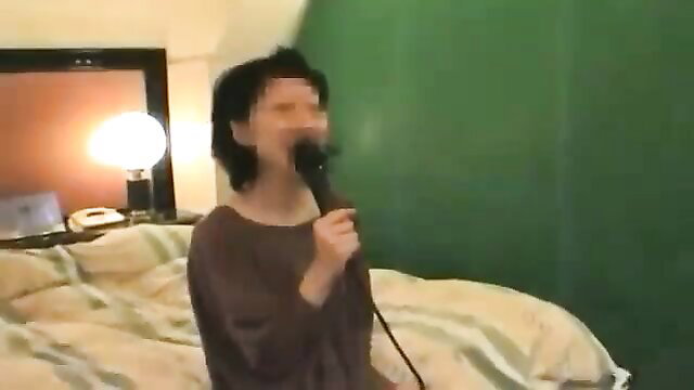 Amateur Japanese woman with short black hair singing into mic on bed in JAV hookup video