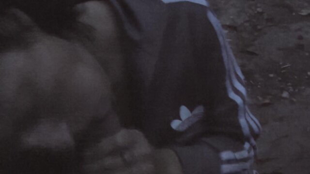 Mystery woman in Adidas tracksuit kneels outdoors, pious swallower pose