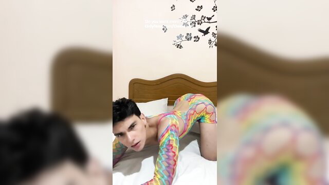 DavelionX in colorful fishnet bodysuit posing seductively on bed