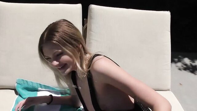 Blonde babe in black slingshot bikini lounging poolside, teasing nude look