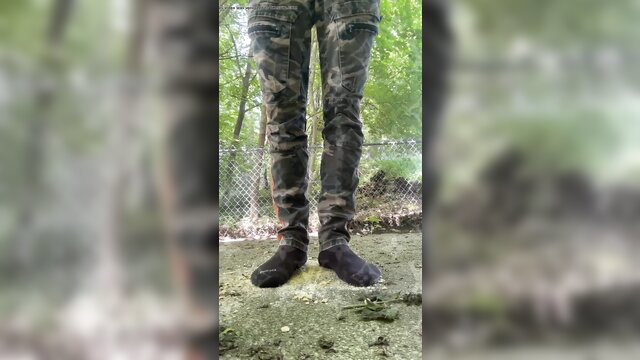 Closeup of woman's camo pants and black socks on dirty ground, giant cracker crush fetish