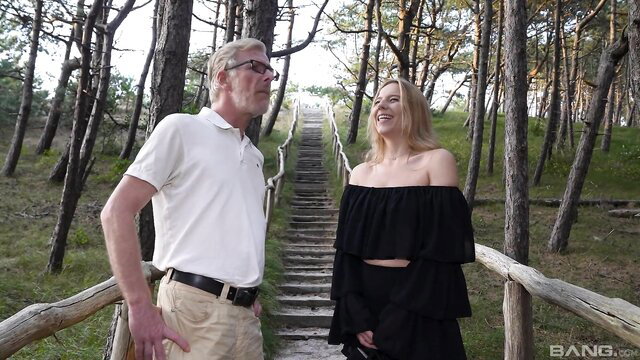 Blonde teen in off-shoulder dress with older man on wooded stairs