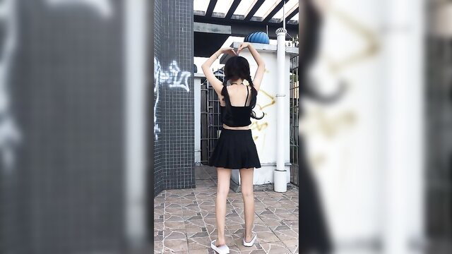 Slim Asian teen in black crop top and mini skirt poses outdoors, sexy back view