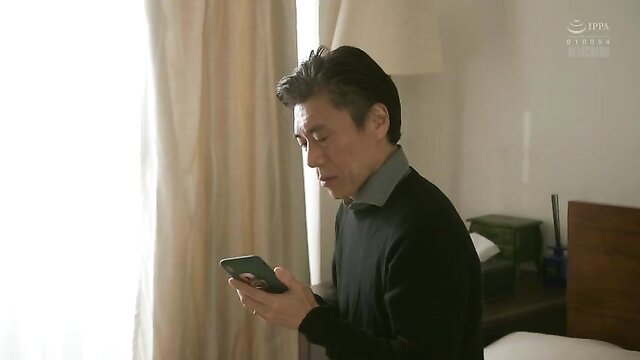 Japanese mature man in sweater holding phone, soft lit bedroom scene