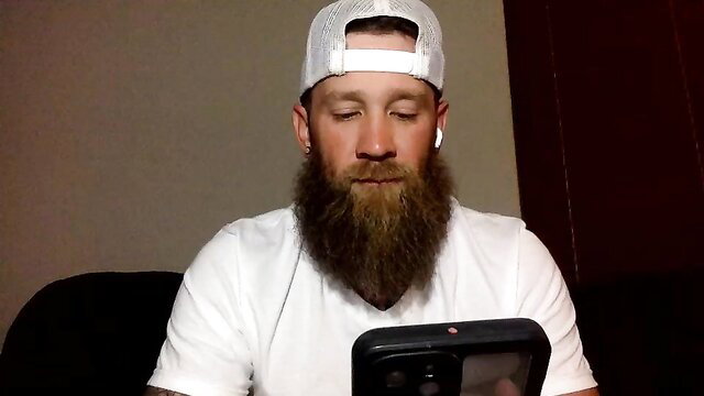 Bearded white guy in white cap and tee holds phone in gay interview thumbnail
