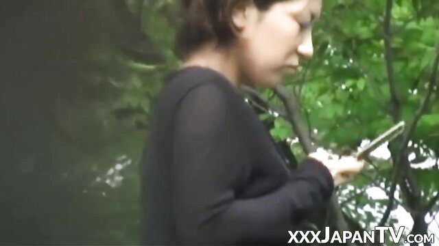 Asian woman in sheer black top holds phone in woods spycam
