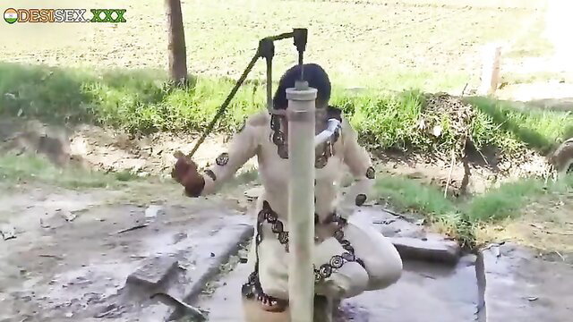 Young Desi girl in white salwar pumping water at handpump outdoors