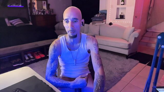 Bald tattooed Latino guy in tank top sits for gay group sex video