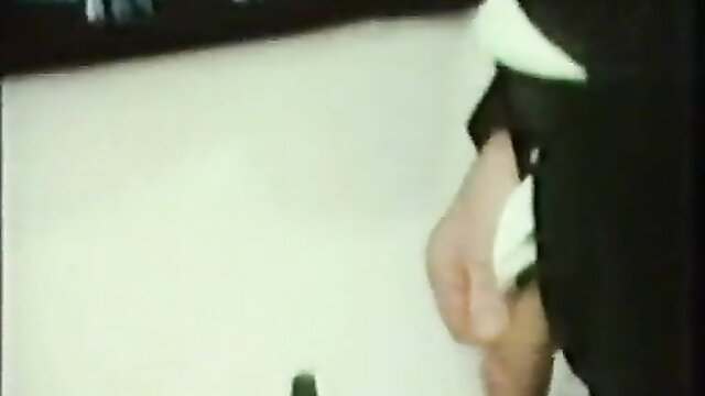 Vintage Golden Geissel piss scene: gloved hand holds cock over white surface