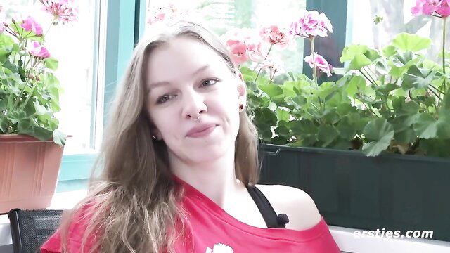 German student Matilda smiles teasingly in red top by window plants