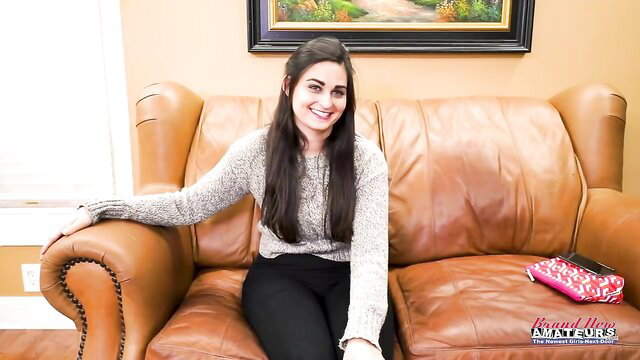 Smiling brunette amateur on leather couch in sweater and leggings