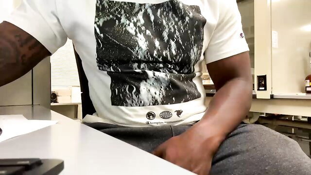 Muscular black guy in Champion tee and sweats sits at desk, gay boyfriend tease