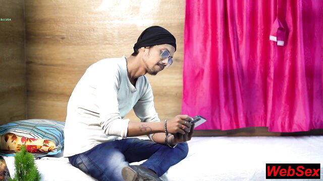 Indian man sitting on bed, looking at phone