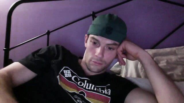 Hot white guy in Columbia tee and green beanie lounges on bed in gay amateur video