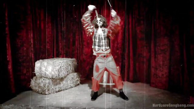 Circus freak slut in clown makeup dances on hay bales in red curtain tent