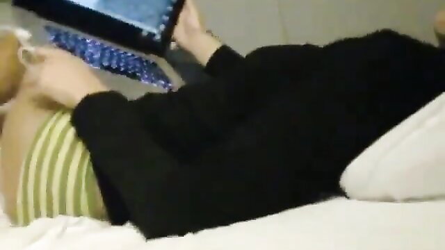 Asian girl in striped top and black sweater lying on bed using laptop