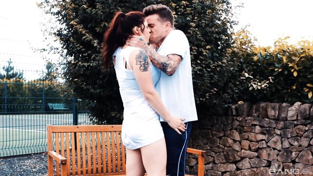 Redhead in white tennis outfit passionately kisses tattooed coach outdoors