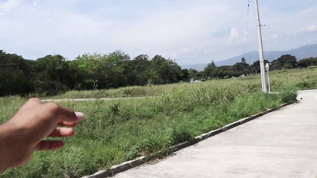 Hand pointing at grassy field with mountains, sunny day outdoors