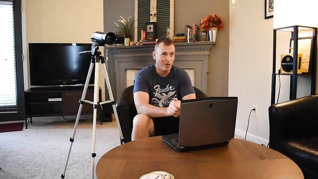 Muscular bald man sits casually in t-shirt with laptop and camera