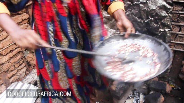Ebony woman in colorful African dress stirs food over fire