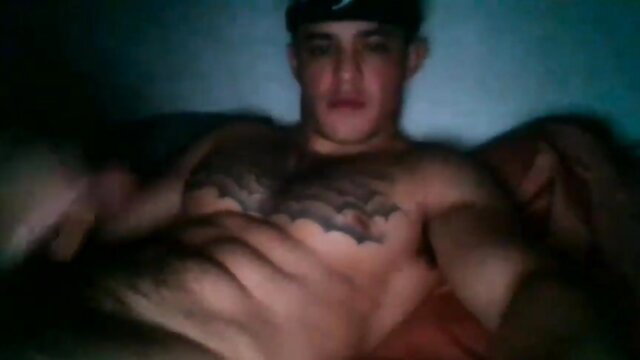 Tattooed muscular Latino guy shirtless on cam, low light flexing abs