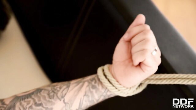 Stacey Saran ties submissive man's tattooed arm with rope in BDSM scene