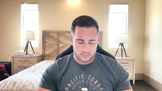 Fit white guy in Pacific Coast tee sits eyes closed on bed masturbating