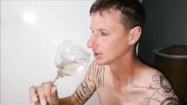 Tattooed white man shirtless sniffing wine glass in golden fun tease