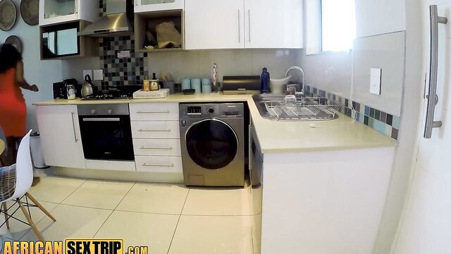 African housewife in red dress bends over kitchen counter