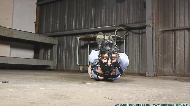 Bound rights activist in leather hood and straps, hogtied on floor
