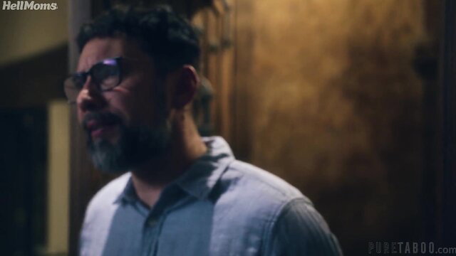 Handsome bearded Latino man in glasses smirking in dim lit room