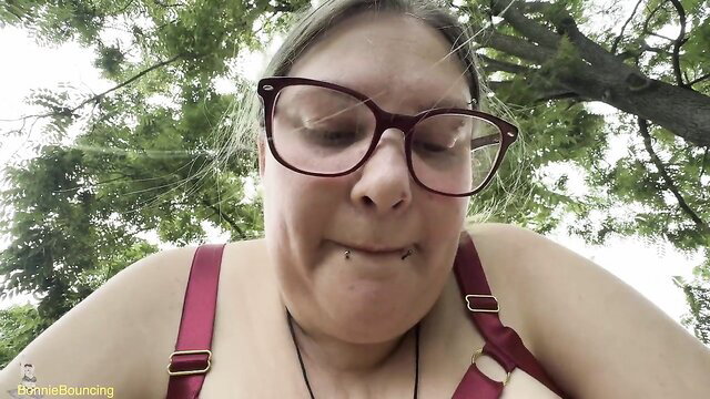 Curly-haired BBW in red lingerie smiling under tree, teasing outdoor