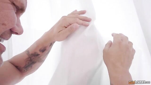 Tattooed man gripping white curtain passionately, intense closeup