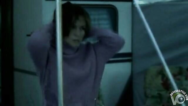 Brunette in purple sweater grabs poles in dim RV nudist scene