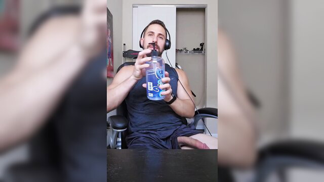 Muscular man in tank top sips from bottle at desk, solo tease