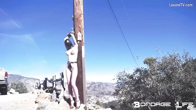 Rachel Greyhound bound to pole outdoors in chastity, nude BDSM
